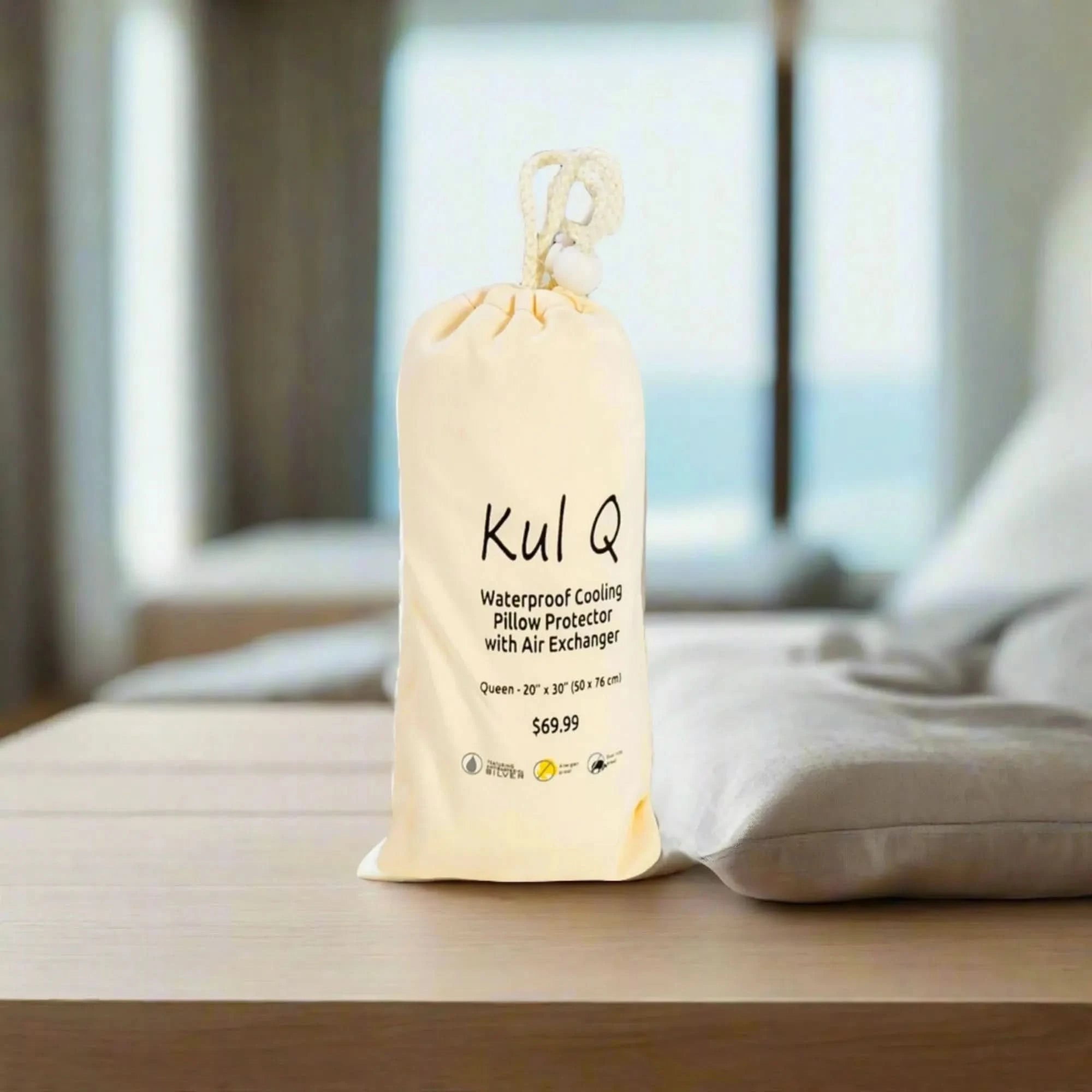 Kul Q Queen waterproof cooling pillow protector in a cream drawstring bag on a wooden surface.