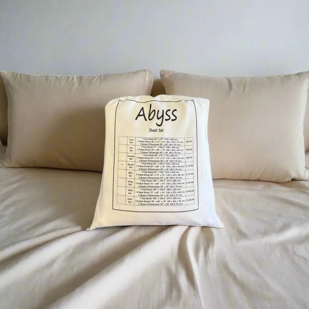 Abyss Microfibre Sheet Set in a light beige color, folded in its white fabric bag with size chart, on a bed.